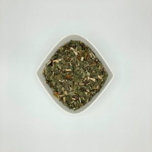 Der Kräutertee Blasendusche befindet sich in einer weißen, rautenförmigen Porzellanschale und besteht aus kleingeschnittenen, vorwiegend grünlichen Kräutern und getrockneten Apfelstücken.