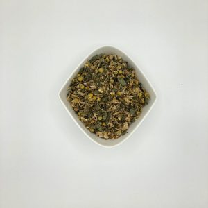 Die weiße rautenförmige Porzellanschale enthält eine Mischung graugrüner Kräuter und gelber Blüten.