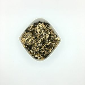 Die weiße rautenförmige Porzellanschale enthält dunkelgrüne, gerollte Blätter und gelbweiße faserige, grobgeschnittene Wurzelstücke.