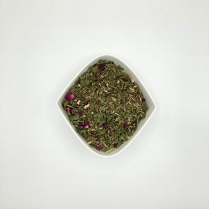 Die weiße rautenförmige Porzellanschale enthält vorwiegend mittelgrüne Blattfragmente, gelblbräunliche Wurzelstücke und einige Rosenblütenblätter.